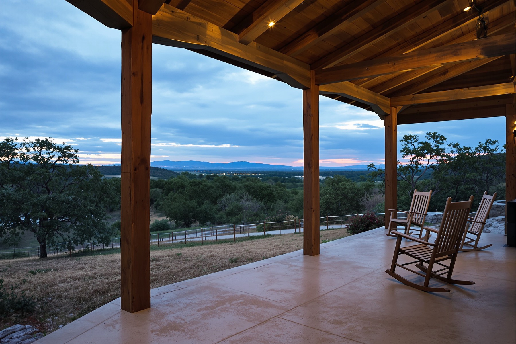 Covered cedar porch with rocking chairs looking over a valley of live oaks at dusk